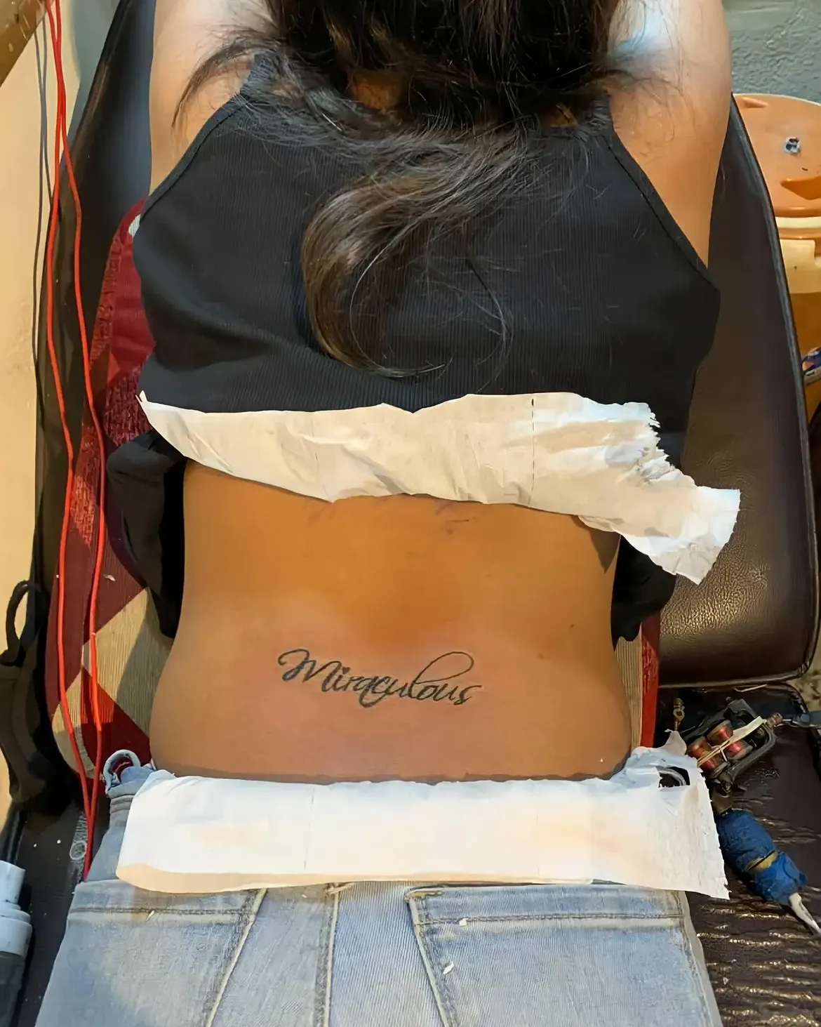 Custom script lettering tattoo reading Miraculous on the lower back, done at Sid Ink Tattoo Delhi